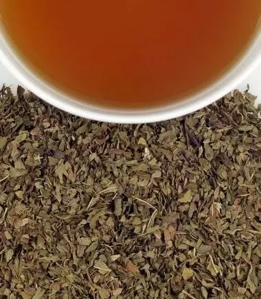 Photo divisée en deux: Copeaux de la Tisane Peppermint Herbal Harney & Sonsen bas et demie tasse remplie de thé en haut