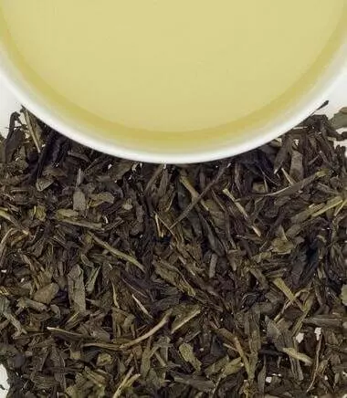 Photo divisée en deux : Copeaux de thé vert Cherry Blossom d'Harney & Sons en bas et demie tasse remplie de thé en haut, vu du dessus