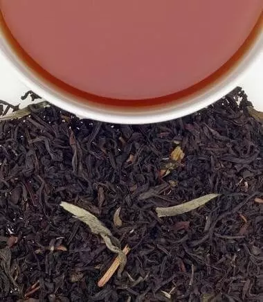 Photo divisée en deux : Copeaux de thé noir Earl Grey Supreme d'Harney & Sons en bas et demie tasse remplie de thé en haut