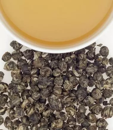 Photo divisée : Copeaux de thé vert Dragon Pearl Jasmine d'Harney & Sonsen bas et demie tasse remplie de thé en haut